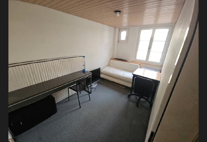 A room with a couch, two tables, two chairs, and a radiator by the windows.