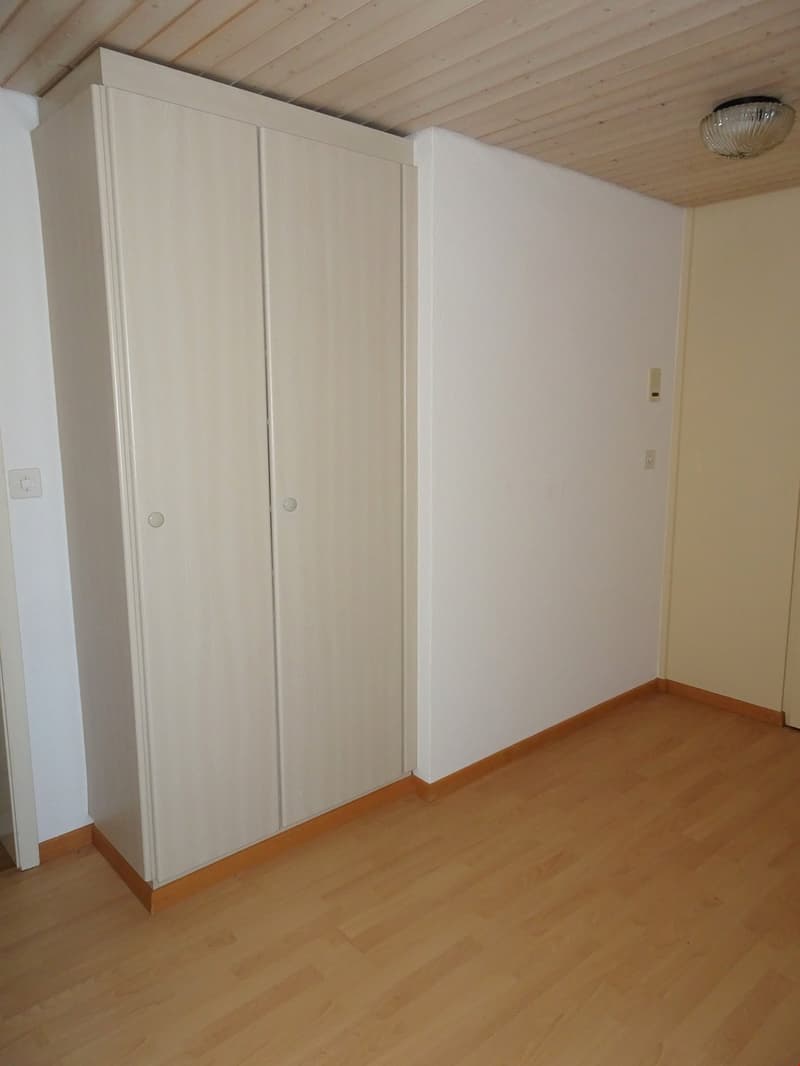 The image shows a bedroom with white walls, a wooden ceiling, and a large built-in wardrobe along one wall. The room has a hardwood floor and appears to be empty, ready for furnishing.