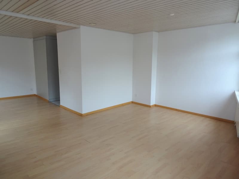 Large open space with white walls, wooden ceiling, and light-colored hardwood flooring. The room appears to be empty, ready for furnishing and decorating.