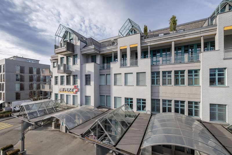 Large building with multiple windows and balconies, with a glass roof over the entrance and underground parking