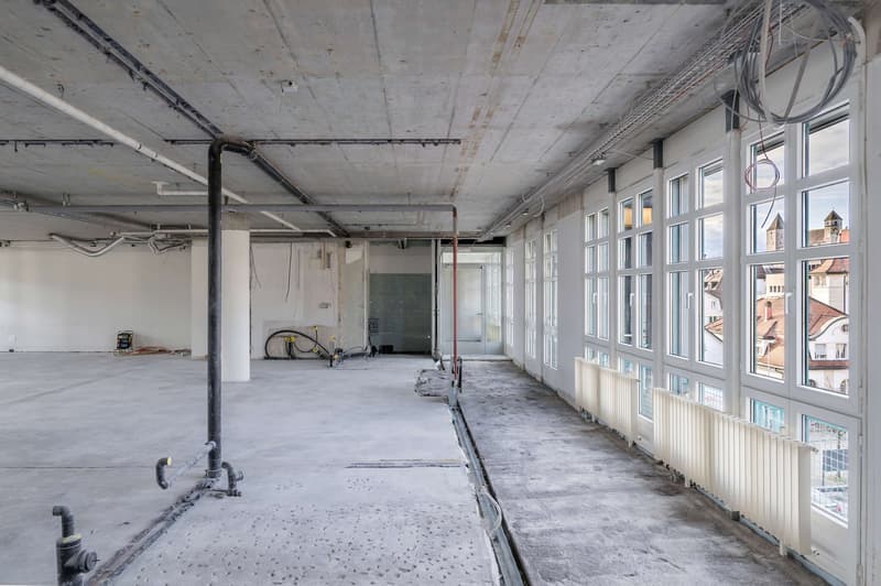 Empty room, large windows, concrete flooring, pipes and metal poles on floor