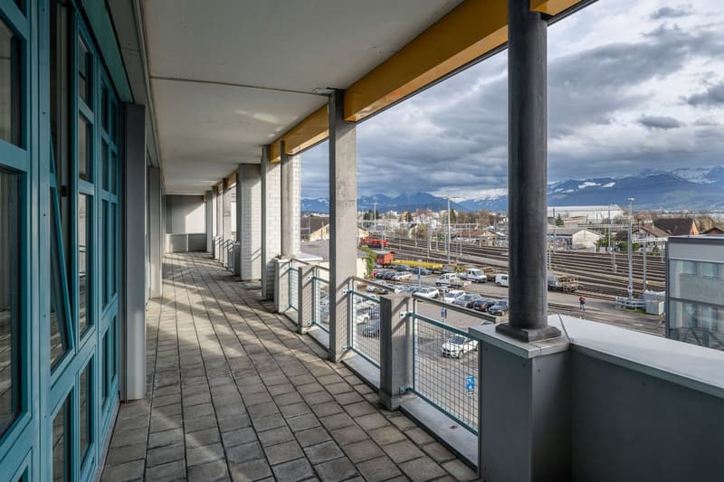 long balcony with tiled floor and metal railings, distant view of mountains and cityscape
