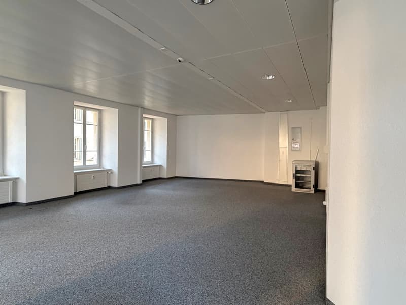 empty room, white walls, gray carpet, three windows, two white cabinets, surveillance camera