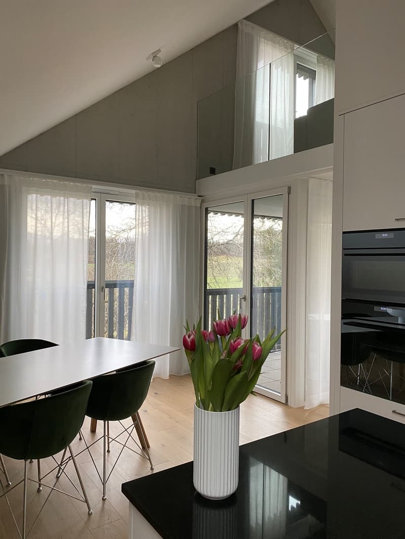 modern kitchen with dining area, white table, green chairs, white vase with pink flowers, glass doors, balcony, white curtains, wooden floor