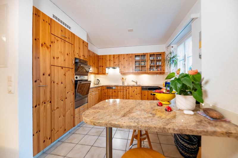 modern kitchen with wooden cabinets, granite countertop, dishwasher, oven, sink, faucet, potted plant, table, stool, tiled floor
