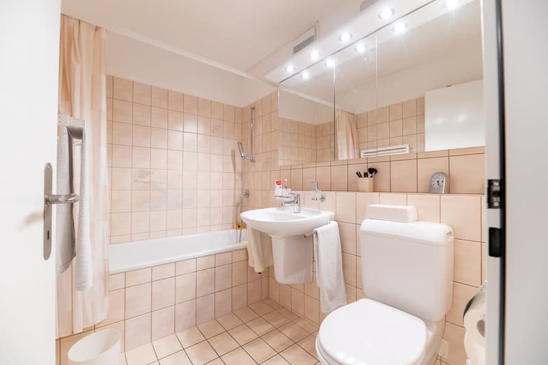 Bathroom with bathtub, sink, toilet, mirror, and tiled walls and floor.