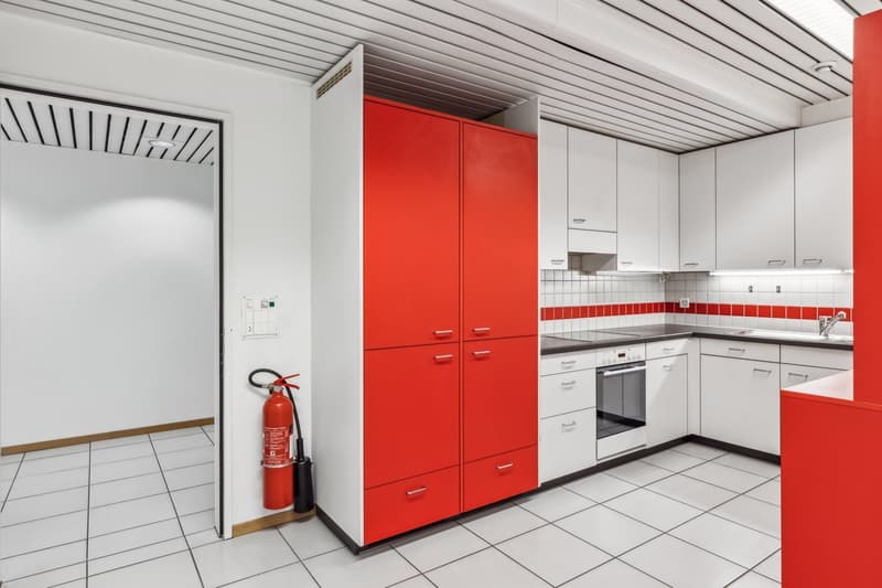 Spacious kitchen with white cabinets, red accent cabinets, tiled floor, and a dishwasher visible