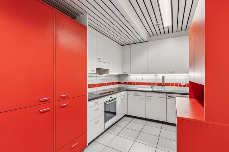 Modern kitchen with red and white color scheme, white cabinets, red tile backsplash, built-in dishwasher, tiled floor