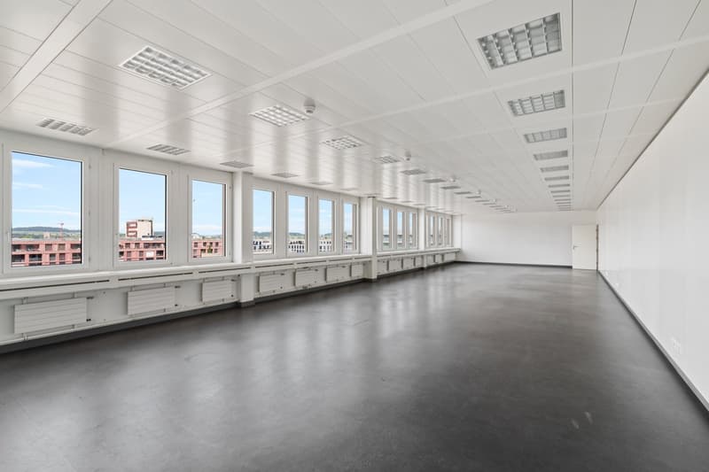 Empty office with gray floor, white walls, multiple large windows with views of the city.