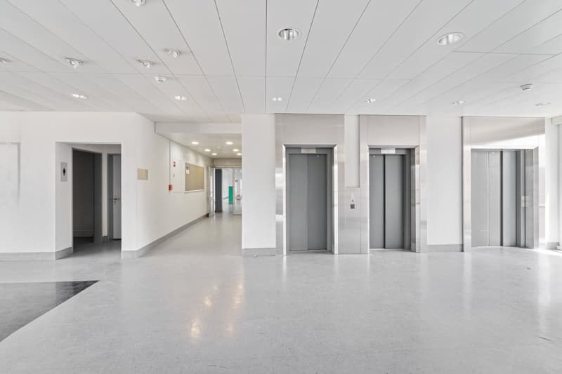 wide hallway, gray elevator doors, white walls and ceiling, empty