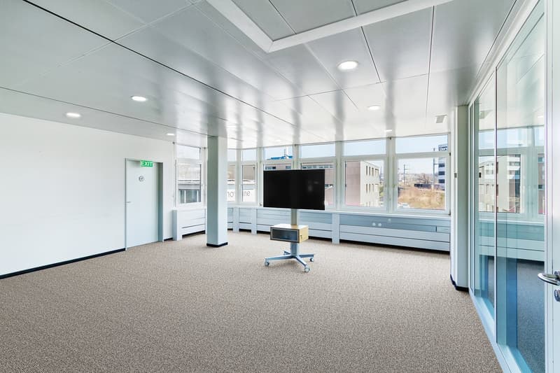 large room with white walls, gray carpet, mounted TV, glass walls, exit door