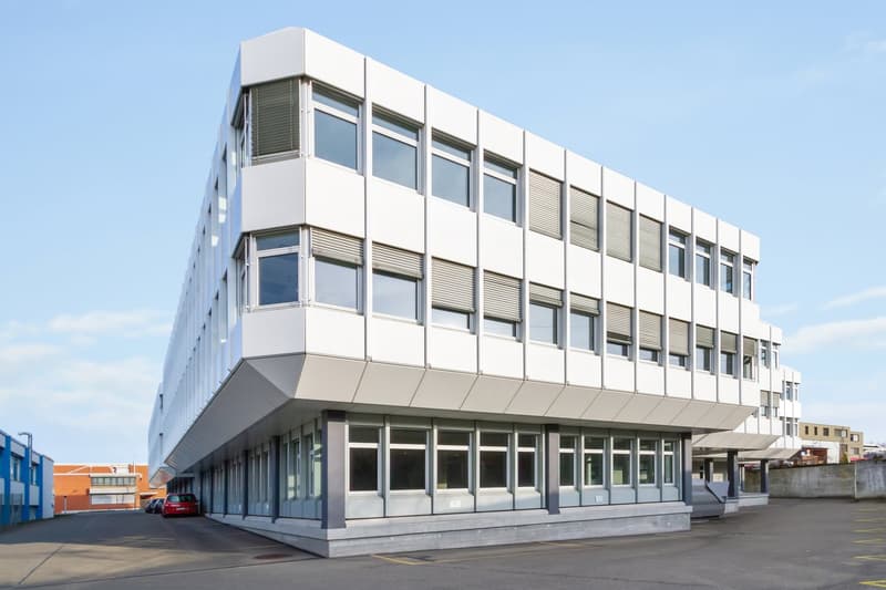 3 story white office building, many windows, parking place