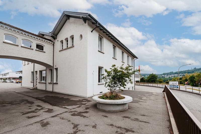 modern building, white painted wall, arched windows, large entrance, parking in front, green view at the back