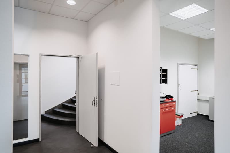empty room with white walls, black floor, two open doors leading to a staircase, small red cabinet in the corner