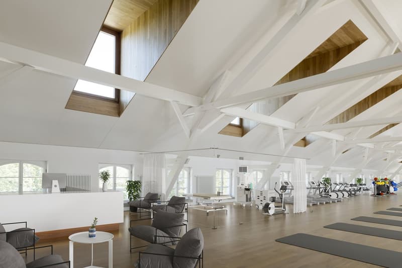 gym room with wooden floor, white walls, wooden beams, windows, exercise equipment, yoga mats, plants, reception desk, chairs, table