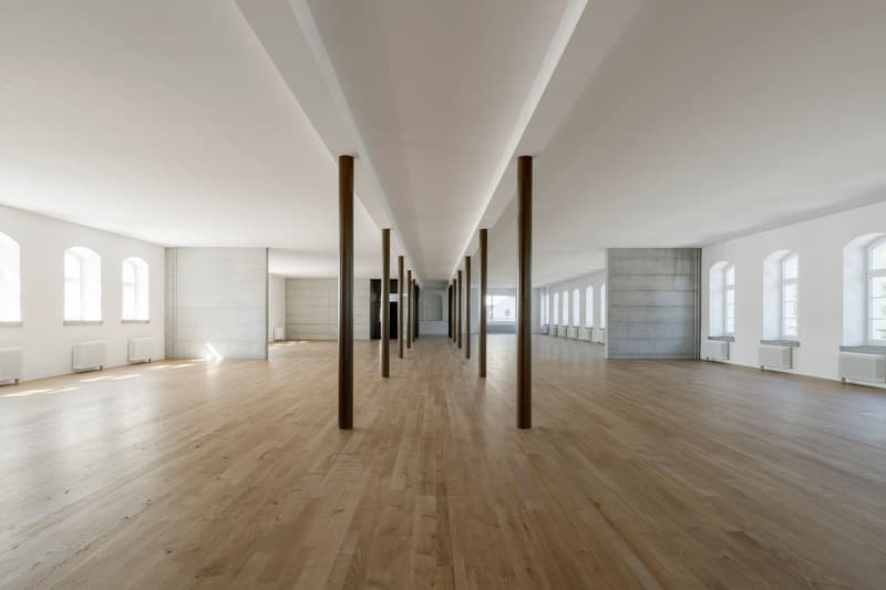 Wide room, wooden floor, white walls, long corridor, white pillars, large arched windows, white radiators