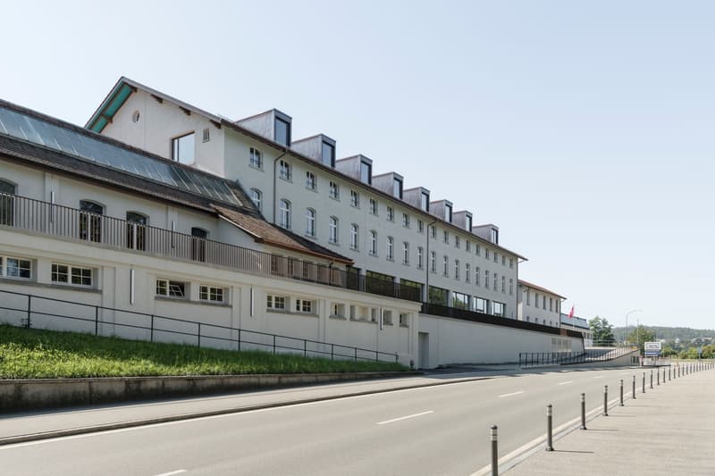 White building with multiple windows, balconies on the second floor, roof with solar panels