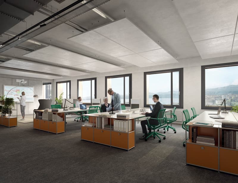 Spacious open office, carpeted floor, desks with shelves, green swivel chairs, large windows, view of mountains, people sitting and standing, office equipment