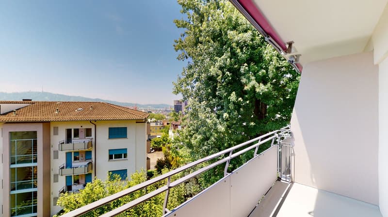 A balcony with metal railing, trees, distant buildings, and mountains in the background