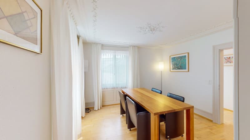wooden dining table, four black chairs, white ceiling, white walls, white curtains, two frames, one lamp, light floor