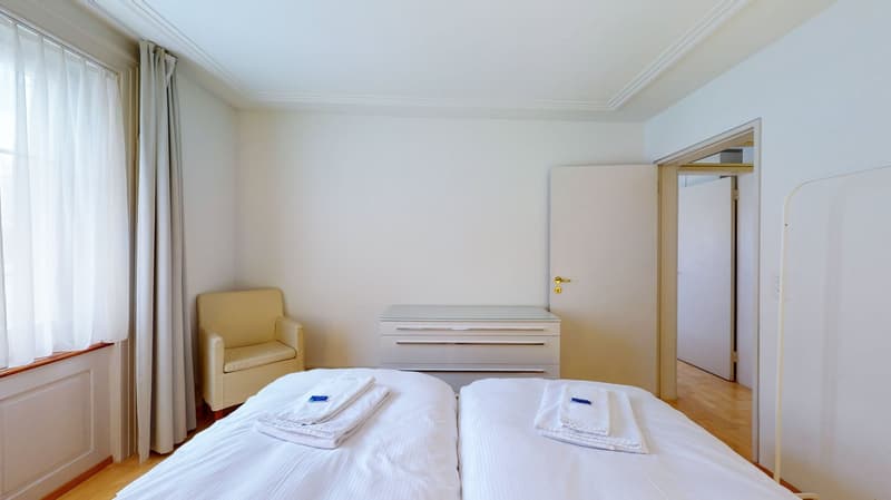 two single beds, window, armchair, white wardrobe, parquet floor