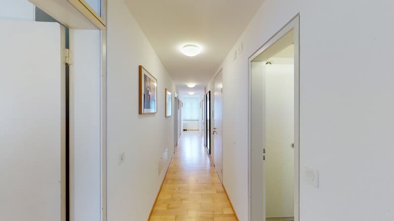 long hallway with white walls, hardwood floor, two doors at the end, ceiling lamps