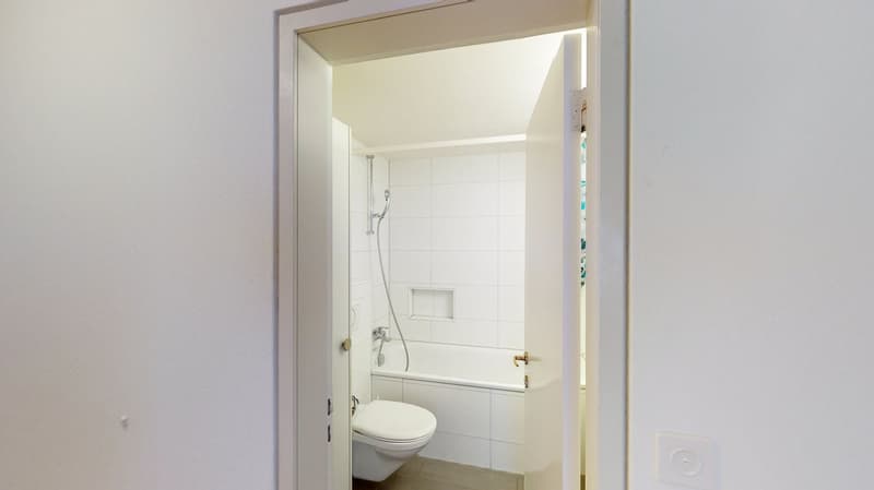 white tiled bathroom with a tub and a toilet, open door