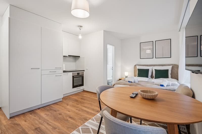 Modern kitchen, dining area, open to bedroom with a double bed, kitchen appliances, decorative pillows