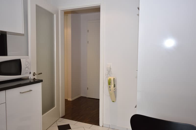 small modern kitchen with microwave, sink, cabinets, white and black tiled floor, wooden floor in another room