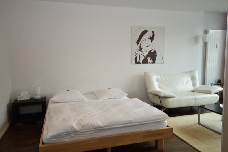 bedroom with double bed, a nightstand with lamps, picture on the wall, a white sofa, a glass table, and a radiator on the wall