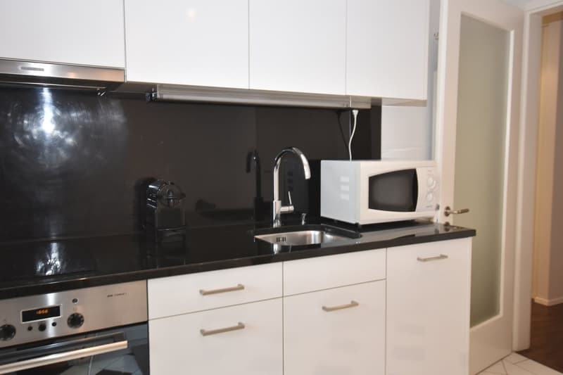 Modern kitchen, black countertop, white cabinets, stainless steel appliances, electric oven, dishwasher, microwave, sink, faucet