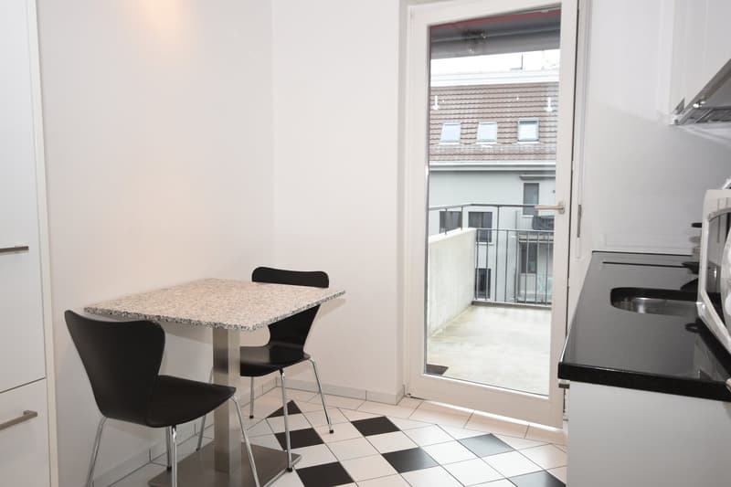 Small kitchen with white walls and black and white tiled floor, marble topped table with 2 chairs, open door to balcony