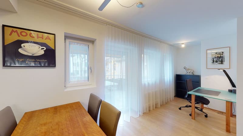 Desk with office chair, dining table with chairs, windows, white walls, paintings, light hardwood floors