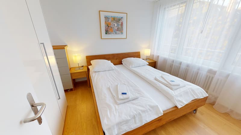 Double bed, white bedding, nightstands with lamps, wooden floors, window with white curtains