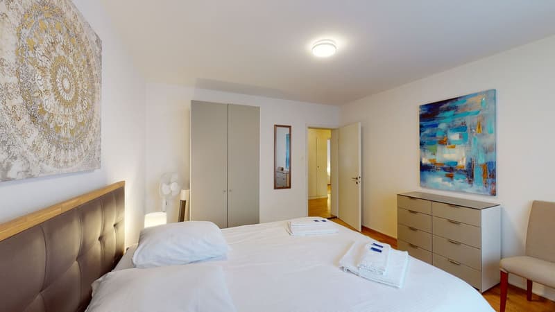 King size bed, pillows, towels, wooden floor, two doors, cabinets, paintings, mirror, fan, lamp