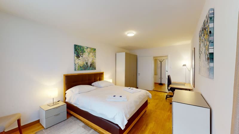 Bedroom: white walls, wooden floor, beige bed, white bedding, nightstand with lamp, open closet, picture frame, desk with chair