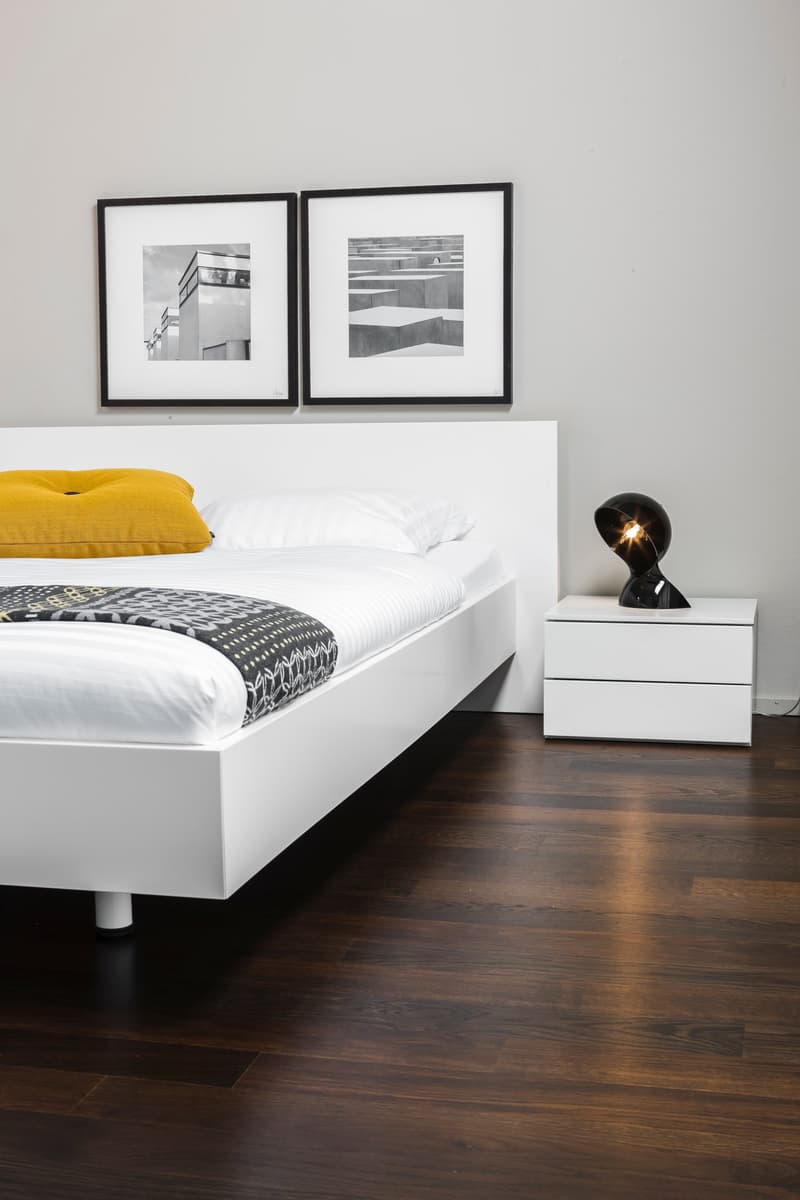 white bed frame, white headboard, white nightstand, white floor lamp, wooden flooring, two framed pictures on wall