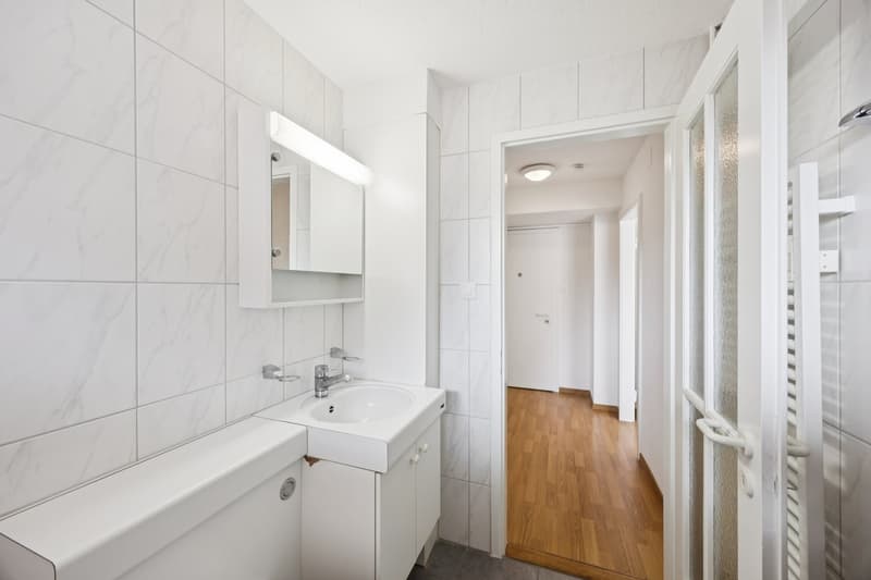 Bathroom with white tiles, white cabinet, sink, mirror, and toilet.