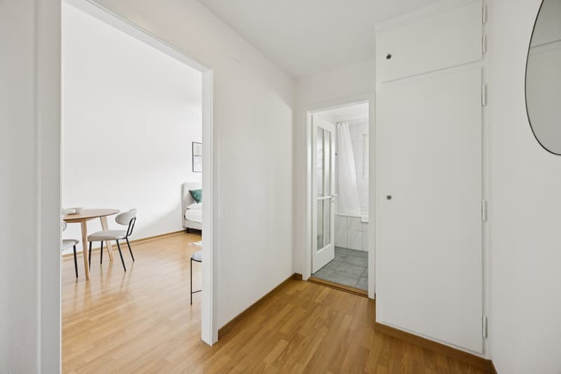 Dining area with table and chairs, wooden floor, bathroom with shower, doorway leading to bedroom
