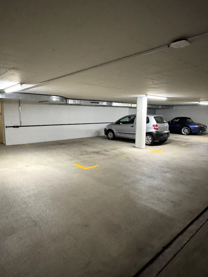 underground parking lot, two cars parked, white walls, yellow parking lines