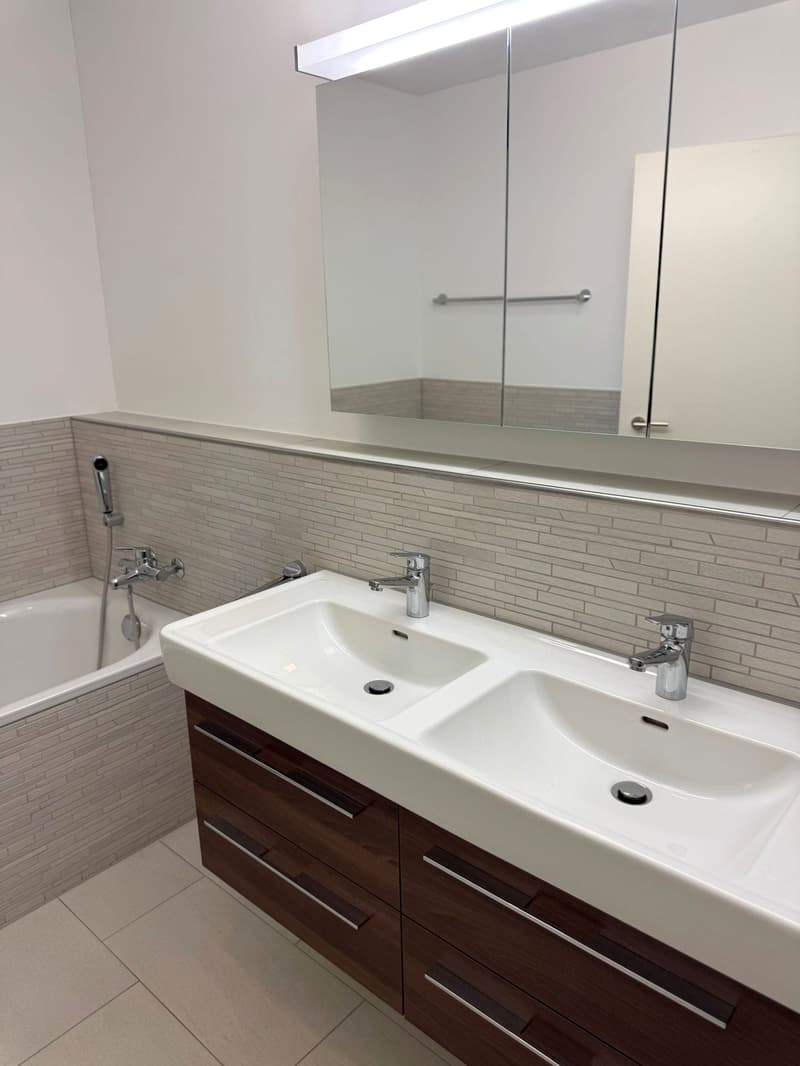 modern bathroom with double sink, bathtub, large mirror, wooden cabinets, tiled floor