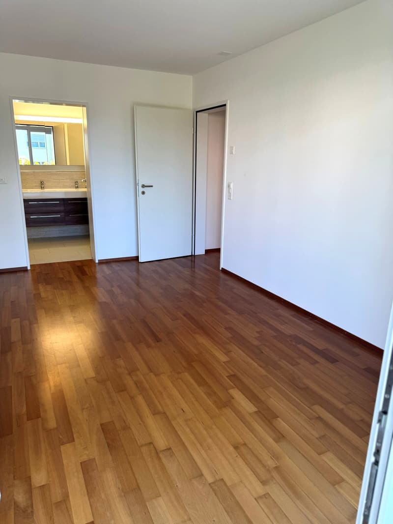 empty room, wooden floor, white walls, white door, bathroom visible in the background