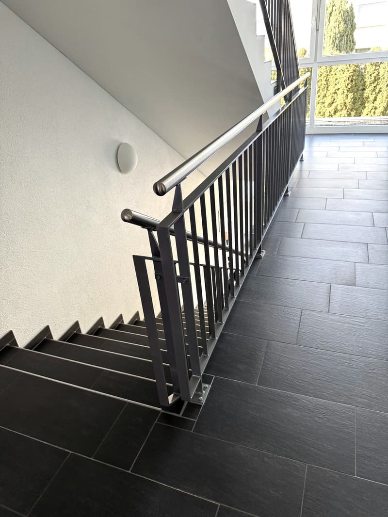 Modern staircase with black tiled steps and a silver handrail