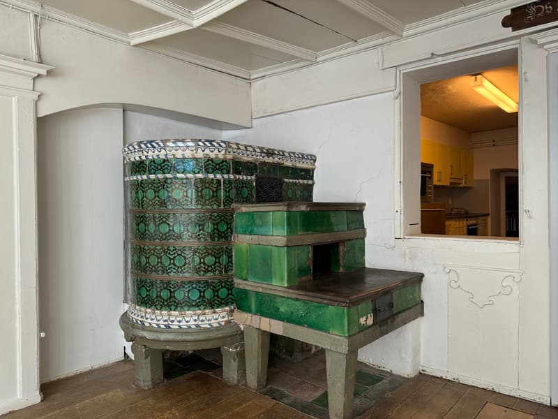 green tiled fireplace, wooden floor, white walls, doorway to kitchen, white trims