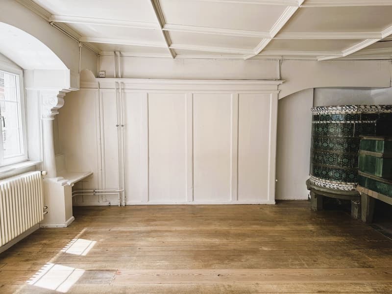 white walls, wooden floors, white radiator, window, two wooden doors