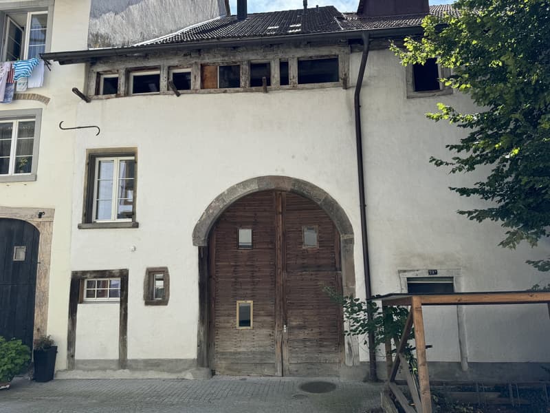 A three story building with wooden windows, wooden door, plants outside, paved front area, chimney