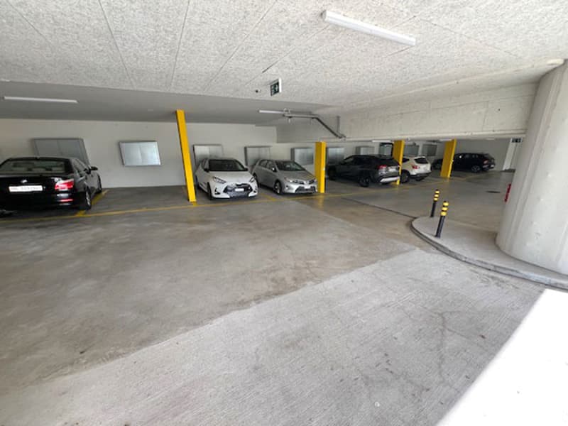 Underground parking garage with white concrete floors, gray pillars, yellow markings, and a white ceiling with lights