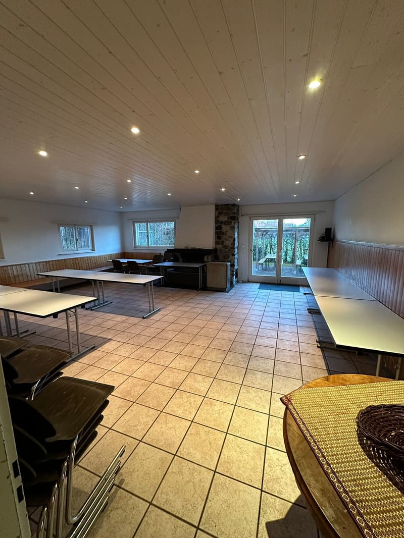 large open room with tables, chairs, and windows, fireplace, kitchen area, and sliding glass doors