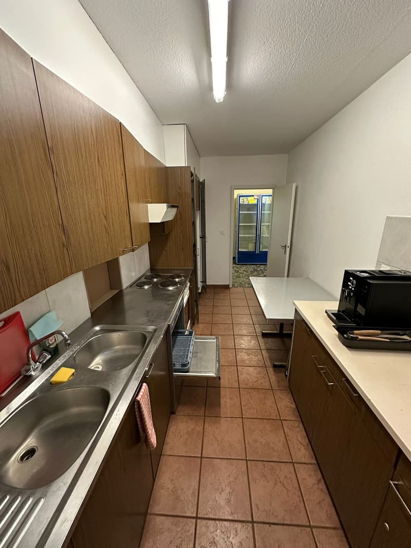 empty kitchen with wooden cabinets, brown tiled floor, stainless steel sink, gas stove, open dishwasher, wooden table, refrigerator