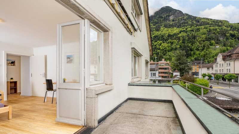 balcony with railings, wooden floor, glass sliding door, small desk, chair, bed, shelves, framed picture on wall